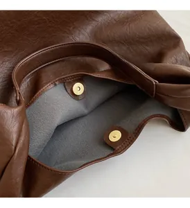 Détail du sac en cuir marron montrant les fermoirs aimantés dorés et la doublure grise