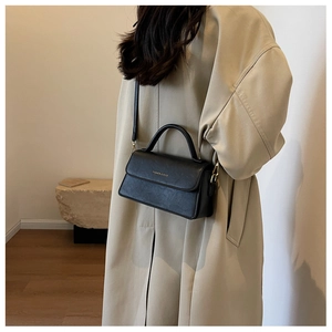 Minimalist black leather handbag on a trench coat model for commute fashion style