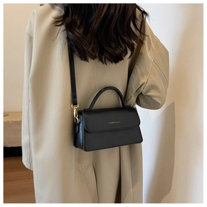Detail of a black leather crossbody bag with gold hardware worn over a beige coat