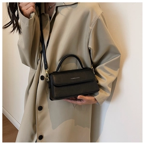 Detail of minimalist black crossbody bag with gold hardware worn on a trench coat