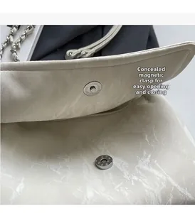 Detail of off-white textured shoulder bag featuring a silver magnetic clasp closure