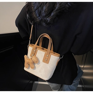 Détail du sac bandoulière crème avec motifs en relief et breloque chien marron