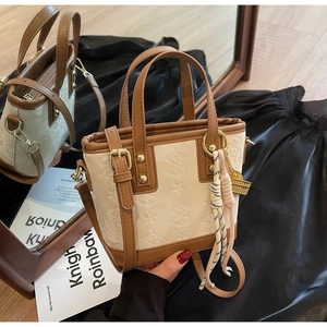 Dettaglio della borsa a secchiello in PU crema con logo a rilievo e ciondolo intrecciato