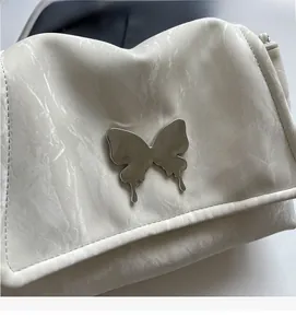 Detailed close-up of cream tote bag with marble texture and large metal butterfly accent