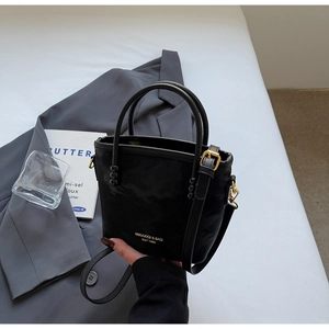 Detailaufnahme der schwarzen matten Beuteltasche mit Goldlogo auf grauem Anzug
