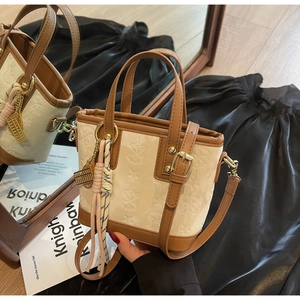 Dettaglio della borsa a secchiello crema con goffratura a stelle e manici marroni