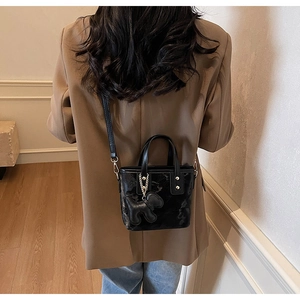 Détail d'un sac seau noir brillant avec texture vintage et breloque chien amovible