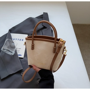 Detailaufnahme der cremefarbenen Beuteltasche mit braunem Rand und goldenem Logo