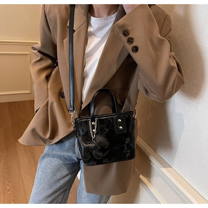 Détail d'un mini sac seau noir brillant avec breloque porté sur un blazer beige chic