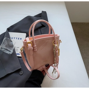 Detailansicht der rosa Lackleder-Handtasche mit goldener Hardware auf einem grauen Blazer