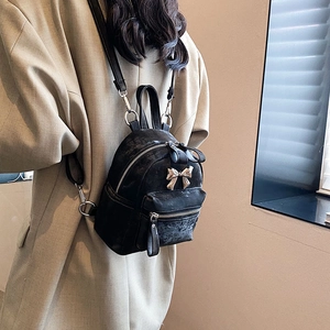 Mini sac à dos noir avec nœud doré porté sur un trench-coat dans un cadre chic