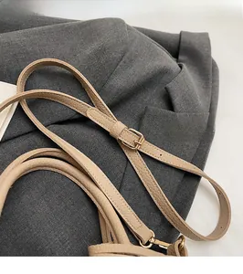 Close-up of adjustable beige leather shoulder strap with gold-tone metal hardware and buckle