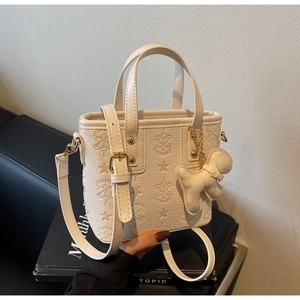 Detail of cream bucket bag with embossed star patterns and astronaut charm accessory