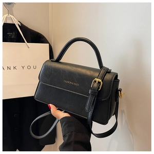Detail of black pebbled leather texture and golden metal buckle on a shoulder bag