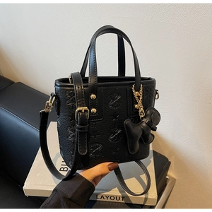 Close-up of black embossed leather bucket bag with golden hardware and bear charm