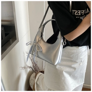 Détail du sac argenté métallisé avec breloque nœud en perles et pendentif cœur
