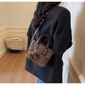 Détail d'un sac seau marron foncé avec motifs floraux en relief et breloque ours
