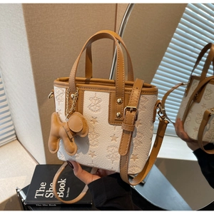 Detailed shot of white embossed bucket bag with brown trim and cute puppy charm