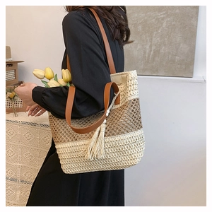 Detail of woven straw tote bag with brown leather straps and decorative tassel charm