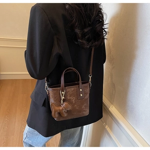 Détail du sac seau en cuir marron foncé avec gaufrage floral et charm de chien