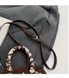 Dettaglio borsa in pelle marrone scuro con manico a foulard e tracolla regolabile