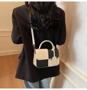 Detail of color-block square bag with handle and brand tag on black blazer