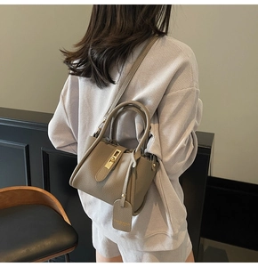 Detail of taupe pebbled leather bucket bag with gold twist-lock and shoulder strap on model