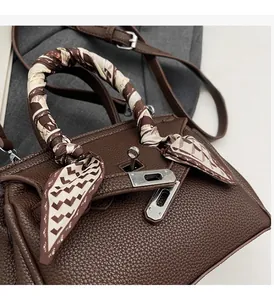 Dettaglio della borsa Kelly in pelle marrone con motivo litchi, foulard e chiusura argento