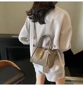 Detail of taupe pebbled leather bucket bag with golden twist lock and cross-body strap