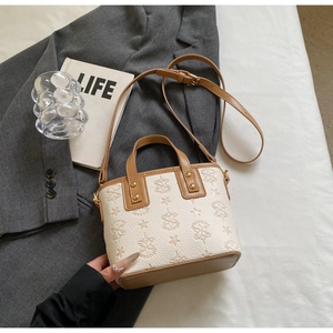 Detail of white litchi grain bucket bag with brown trim and golden hardware