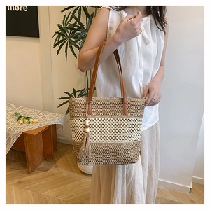 Detail of straw woven tote bag featuring khaki stripes, brown leather handle and fringe tassel