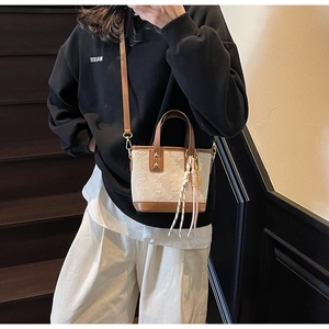 Dettaglio ravvicinato della borsa beige a tracolla con motivi a rilievo e manico marrone