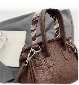 Dettaglio borsa in pelle litchi marrone scuro con manico avvolto da foulard e dettagli in metallo