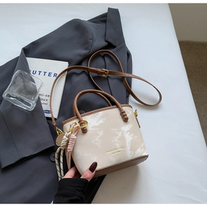 Detail einer beigen und braunen Eimertasche mit Goldlogo auf einem grauen Blazer