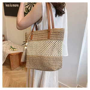Detailansicht der gewebten Stroh-Tasche mit Ledergriffen und Quaste an einem weiblichen Model