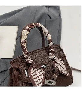 Dettaglio di borsa in pelle marrone con chiusura a scatto in metallo e manico con foulard