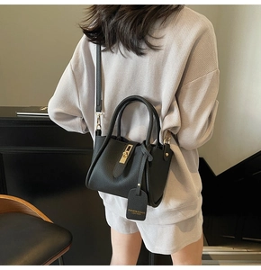 Detailed view of black lychee grain leather handbag with gold metal lock and shoulder strap