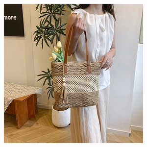 Detail of hand-woven straw shoulder bag with striped texture and decorative tassel