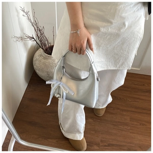 Détail du sac argenté en demi-lune avec nœud à carreaux bleus et pendentif cœur