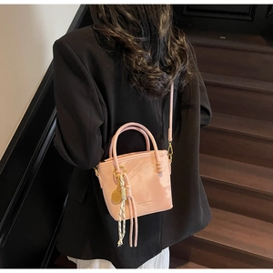 Detailansicht der rosa Beuteltasche mit Goldanhänger und Streifenknoten auf dunklem Grund