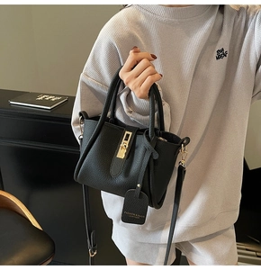 Detailed view of black litchi leather texture with golden twist-lock and fashion tag
