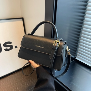 Classic black leather square bag with gold hardware and top handle shown on a desk