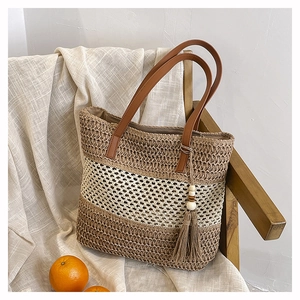 Detail of handwoven straw tote bag with striped pattern, leather handles, and tassel charm