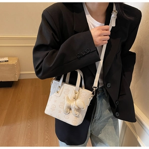 Detail of white star-embossed bucket bag featuring a cute detachable dog charm and gold hardware