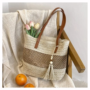 Detailed texture of hand-woven straw tote with brown leather handles and fringe charm