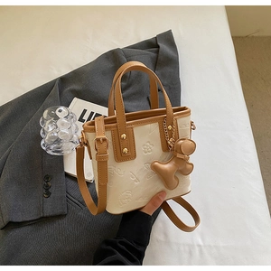 Détail du sac seau en cuir crème avec motifs chiots embossés et pendentif décoratif chic