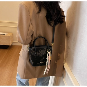 Detailansicht einer schwarzen Lackleder-Eimertasche getragen zu einem braunen Blazer mit Anhänger