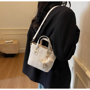 Detailed view of white embossed leather bucket bag with star patterns and plush dog charm