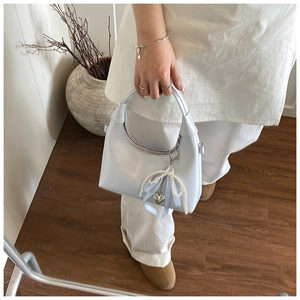 Détail du sac à main en cuir verni bleu clair avec nœud perlé et breloque cœur