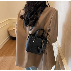 Detail of black embossed leather bucket bag with gold hardware and bow charm on model